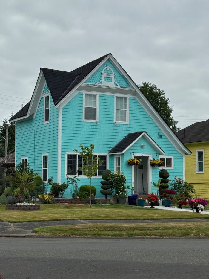 Charming turquoise house with vibrant front garden, showcasing colorful flowers and neat landscaping.