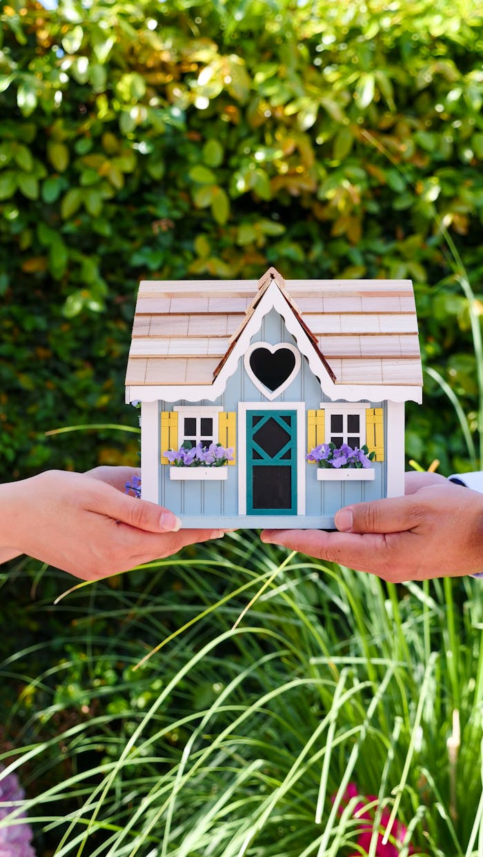 Two hands hold a colorful miniature house outdoors, symbolizing real estate and home ownership.